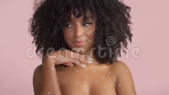 混合种族的黑人妇女卷发被水晶化妆覆盖在粉红色背景的工作室视频的预览图