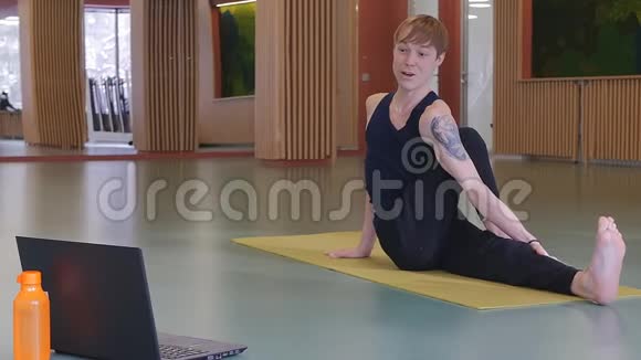 在线瑜伽课程一个年轻英俊的纹身男人正在笔记本电脑前教瑜伽伸展和伸展视频的预览图
