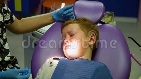 害怕的红发男孩在牙科椅上接待牙医时哭泣儿科牙医视频的预览图