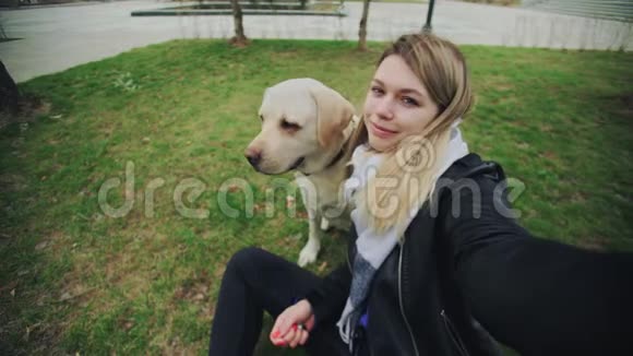 公园里一个年轻的金发女郎和一只猎犬在自拍视频的预览图