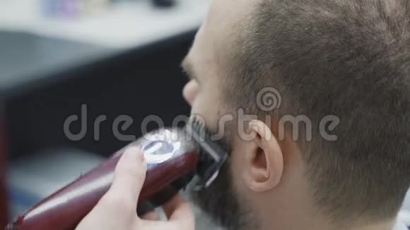 理发店的理发师用剃须机修剪胡须口渴的过程发型师切割术的特写视频的预览图