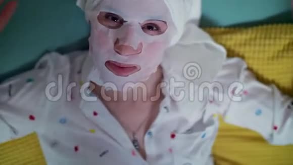 肖像年轻的女士戴着化妆面料面具的女人头上戴着白色毛巾躺在沙发上放松着视频的预览图