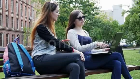 在校园公园坐在长凳上的现代女学生在学生项目上一起使用笔记本电脑视频的预览图