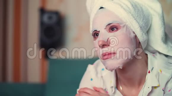 肖像美丽的女人戴着化妆织物面具头上戴着一条白色毛巾在电视屏幕的灯光下视频的预览图