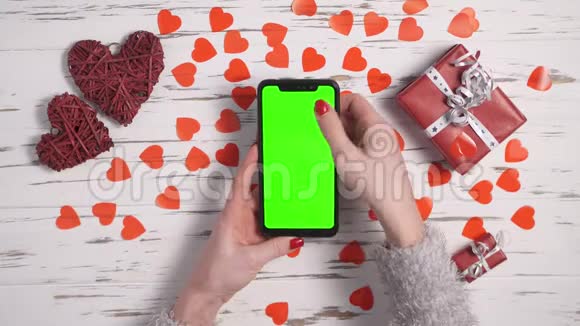 俯视图女性双手使用智能手机在一张装饰有心脏的桌子上视频的预览图
