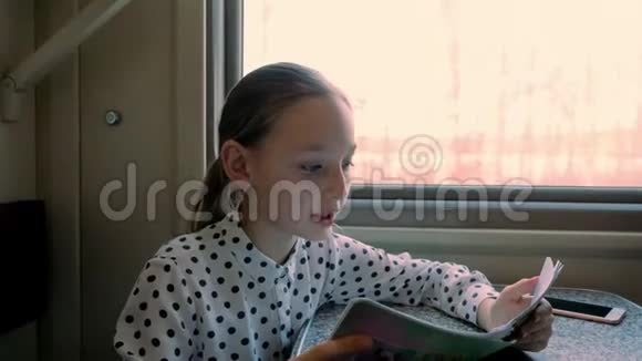 年轻女孩十几岁在窗口背景下一边看火车一个十几岁的旅游女孩在窗边的火车上看书视频的预览图