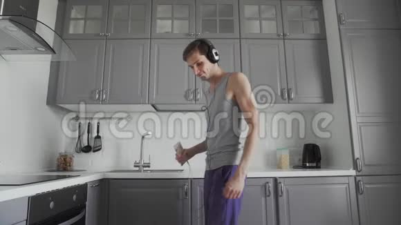戴着耳机的帅气年轻风趣男子早上在家厨房跳舞度假玩得开心视频的预览图