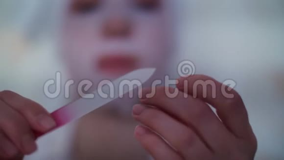 特写镜头一个女人戴着化妆织物面具头上戴着一条白色毛巾用指甲锉视频的预览图