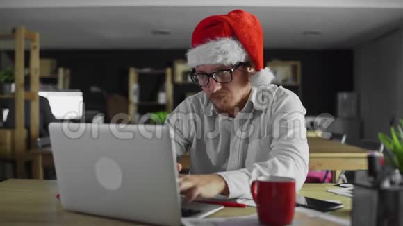 年轻的经理在办公室工作并在圣诞节期间用智能手机讲话视频的预览图
