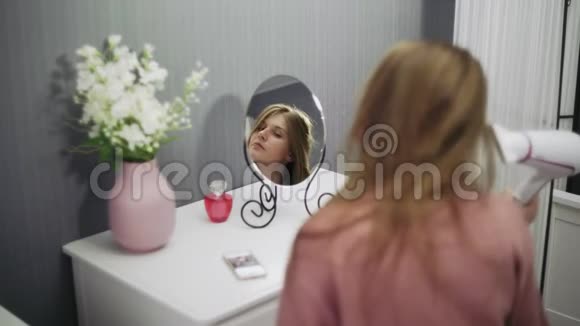 漂亮的年轻女子正在用吹风机照镜子视频的预览图