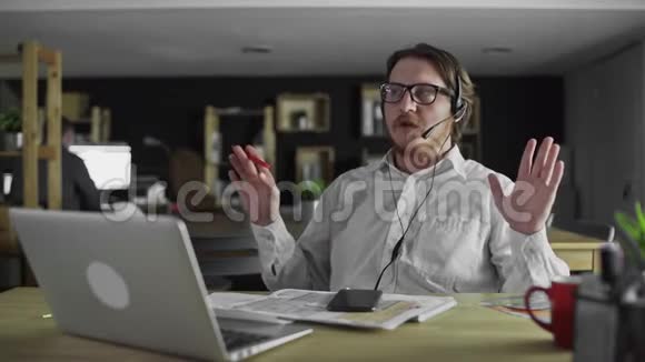戴耳机的年轻经理正在办公室用笔记本电脑工作视频的预览图