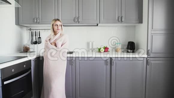 一个裹着毯子的悲伤女孩早上在厨房里喝茶和叹息视频的预览图