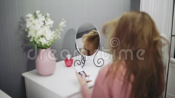 美丽的年轻女子正在使用吹风机和智能手机上网视频的预览图