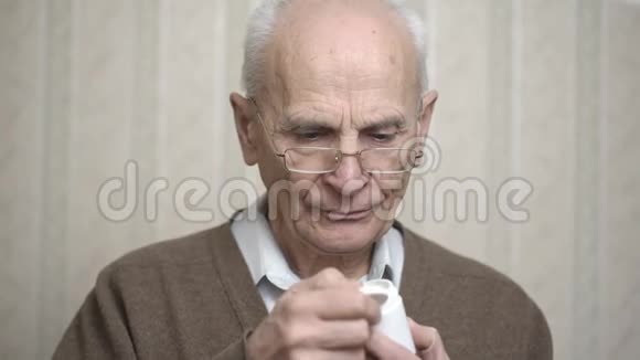 穿棕色夹克的老人打开罐子在房间里吃药视频的预览图