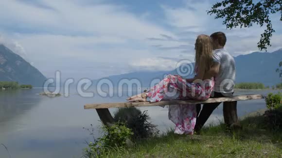 一对夫妇坐在河岸上的长凳上说话看着山视频的预览图