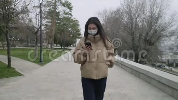 一个美丽的女人戴着口罩在一个空城中心散步打电话在冠状病毒COVID期间视频的预览图