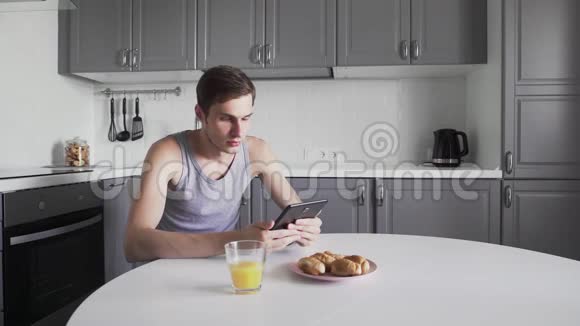 年轻人在家里坐在厨房里用数码平板电脑看新闻视频的预览图