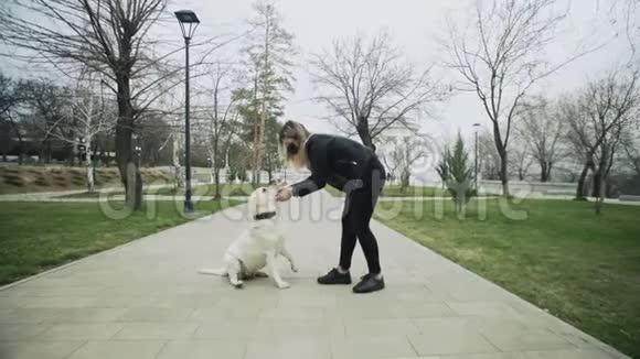 在隔离冠状病毒COVID19期间戴着黑色面具的女人在公园里玩她的拉布拉多犬视频的预览图