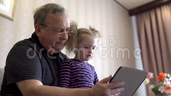 孙女和祖父坐着一块石碑女孩对平板皱着眉头一起坐在沙发上视频的预览图
