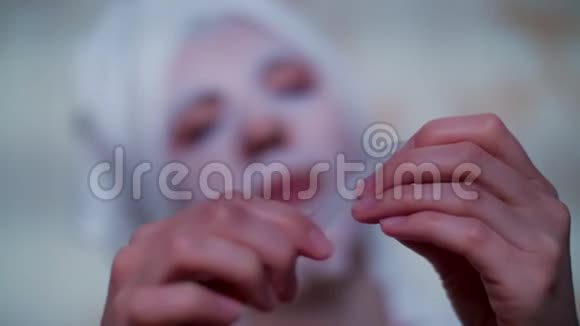 特写镜头一个女人戴着化妆织物面具头上戴着一条白色毛巾用指甲锉视频的预览图