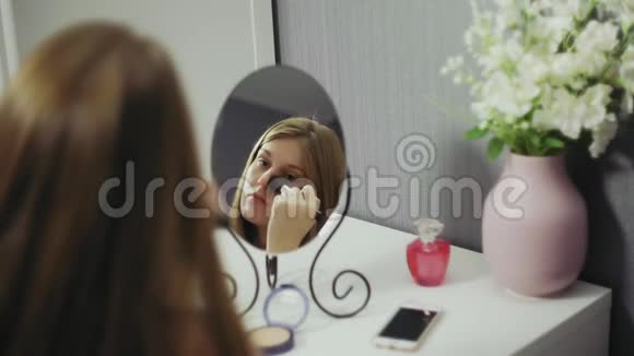 年轻的美女拿着刷子涂上腮红粉在智能手机上聊天视频的预览图