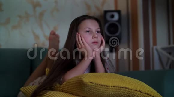穿着睡衣在电视上看电影的十几岁女孩躺在沙发上房间被来自视频的预览图