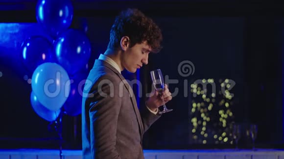 一个穿着休闲服在镜头前闻着一杯香槟的年轻人在一个黑暗的房间里视频的预览图