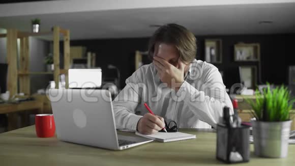 又累又困的经理正在办公室用笔记本电脑工作视频的预览图