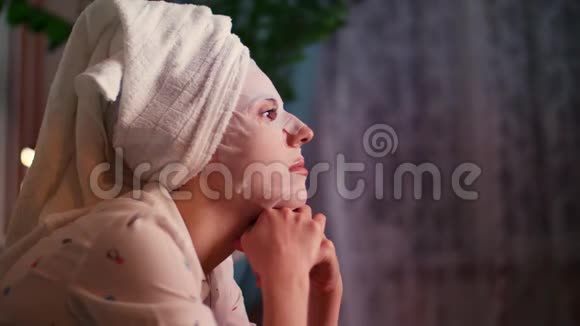 肖像画一位戴着化妆面料面具头上戴着一条白色毛巾的妇女在电视屏幕的灯光下视频的预览图