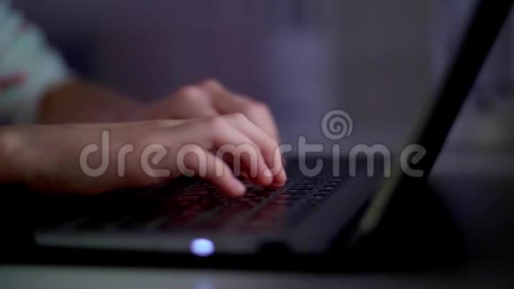 特写一个女孩的手一个孩子正在笔记本电脑键盘上打字在显示器的灯光下晚上视频的预览图