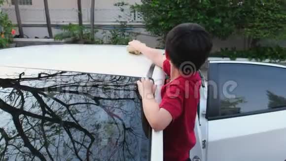 一个亚洲男孩小心地清洗白色汽车上的污垢用黄微纤维清洁车顶视频的预览图