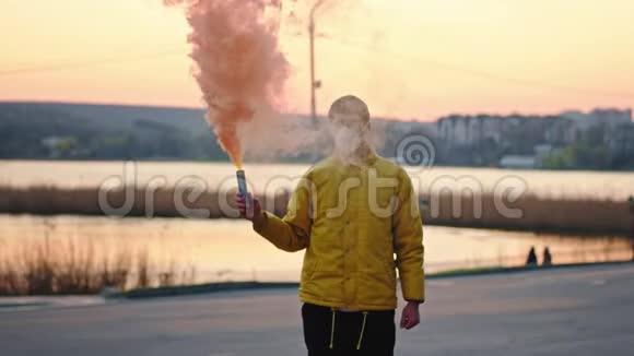 一个戴着防护面罩的年轻人站在大流行病的空旷公园里的摄像机前他举着烟视频的预览图