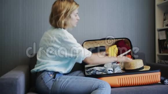 旅行妇女坐在沙发上关上手提箱准备上路旅行的侧景视频的预览图