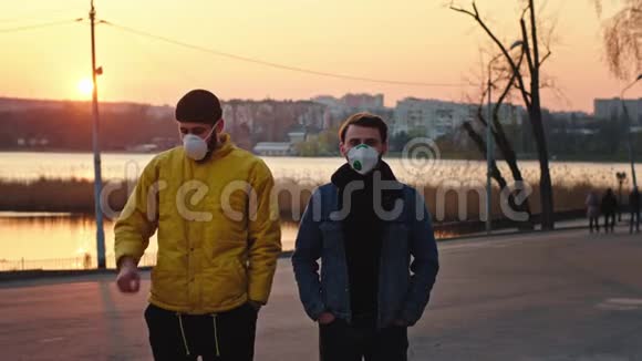 在公园的日落时分两个戴着防护面罩的朋友站在摄像机前咳嗽视频的预览图