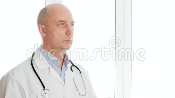 肖像医生穿着白色医用长袍在窗口背景上看着声音筒听诊器治疗师视频的预览图