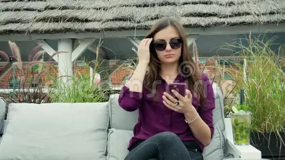 迷人的年轻女性使用手机喝一杯冷的莫吉托鸡尾酒在露台享受美好时光视频的预览图