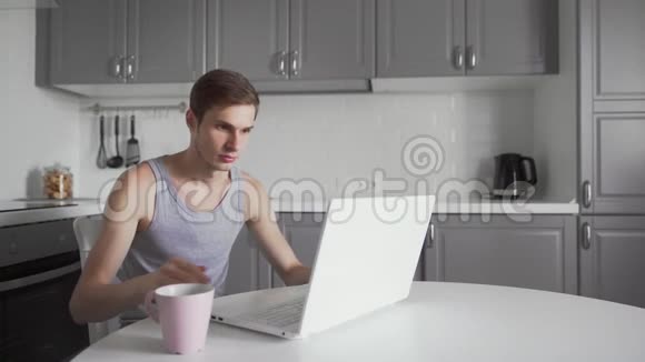 精疲力竭的男人在家喝茶在笔记本电脑上工作厌倦的商人视频的预览图