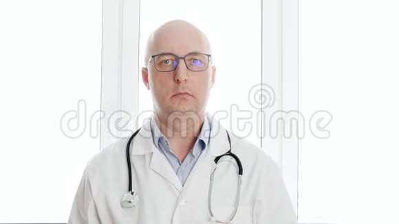 把戴眼镜的医生和穿白色医用长袍的医生关起来看着窗户背景上的摄像机面对面的医生视频的预览图