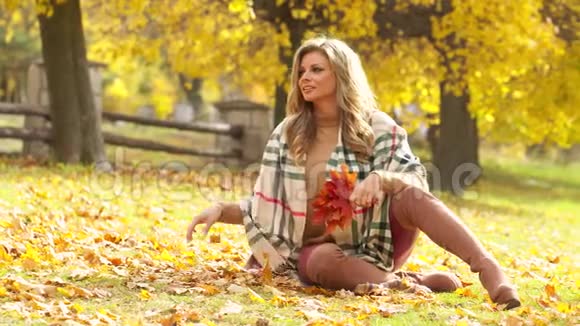 迷人的年轻女子带着性感的微笑坐在秋天的公园里4k视频镜头慢镜头视频的预览图