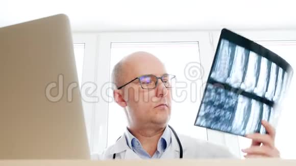 外科医生在医疗办公室里看背骨x光前置笔记本电脑屏幕男性医生检查X光并致力于视频的预览图