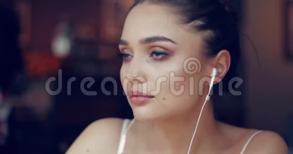 年轻温柔的女孩戴着耳机坐着看着视频的预览图