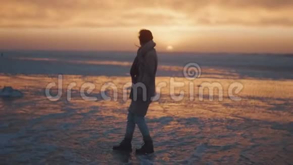 史诗般的海上日落背景快乐的旅游妇女在寒冷的冬天看着海岸上覆盖着泡沫的慢动作视频的预览图