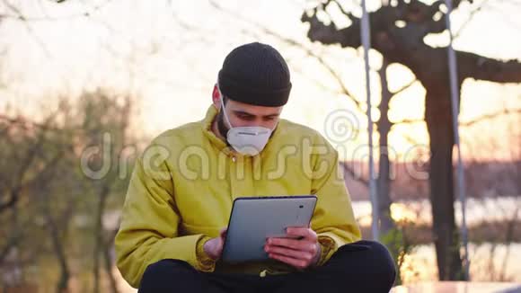 专心致志的人坐在公园的椅子上一边打字一边戴着防护面罩视频的预览图