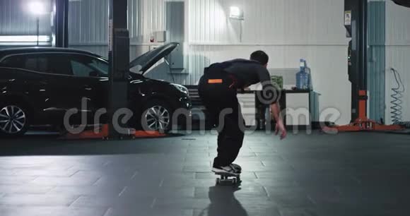 在大型汽车服务中心穿着制服的机械师在工作场所玩滑板玩得很开心视频的预览图