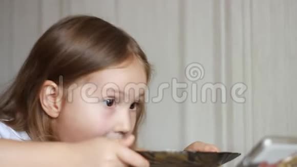 孩子用勺子吃汤在智能手机上看视频贴身女婴坐在家里做饭的桌子旁视频的预览图