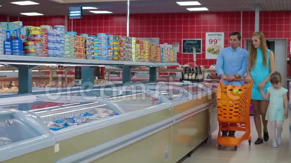 有小女儿的年轻父母在一家大型超市里选择食物人们在杂货店里选择冷冻鱼视频的预览图
