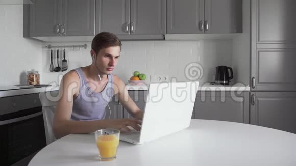 带耳机的年轻自由职业者工作在笔记本电脑上喝果汁视频的预览图