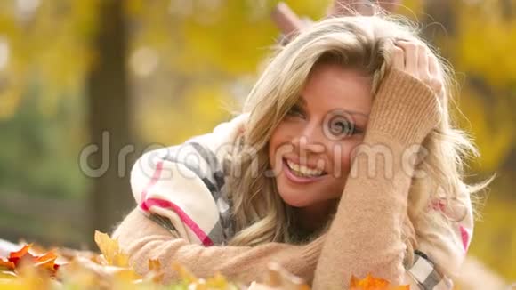 迷人的年轻女子带着性感的微笑躺在秋天的公园里4k视频镜头慢镜头视频的预览图