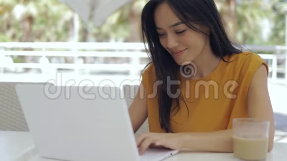 可爱的混血女人坐在户外自助餐厅桌上用笔记本电脑视频的预览图