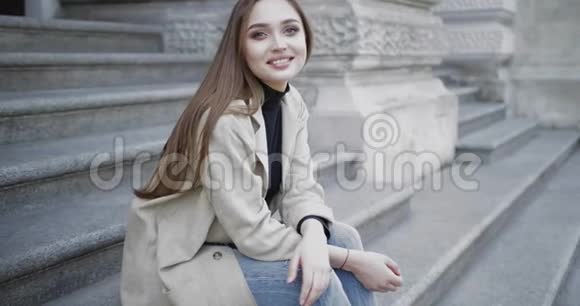 年轻时尚的女性穿着牛仔裤和外套对着镜头微笑视频的预览图